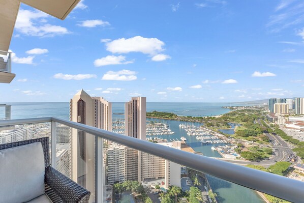 Un balcon offrant une vue sur un port de plaisance, de grands immeubles et un ciel dégagé.