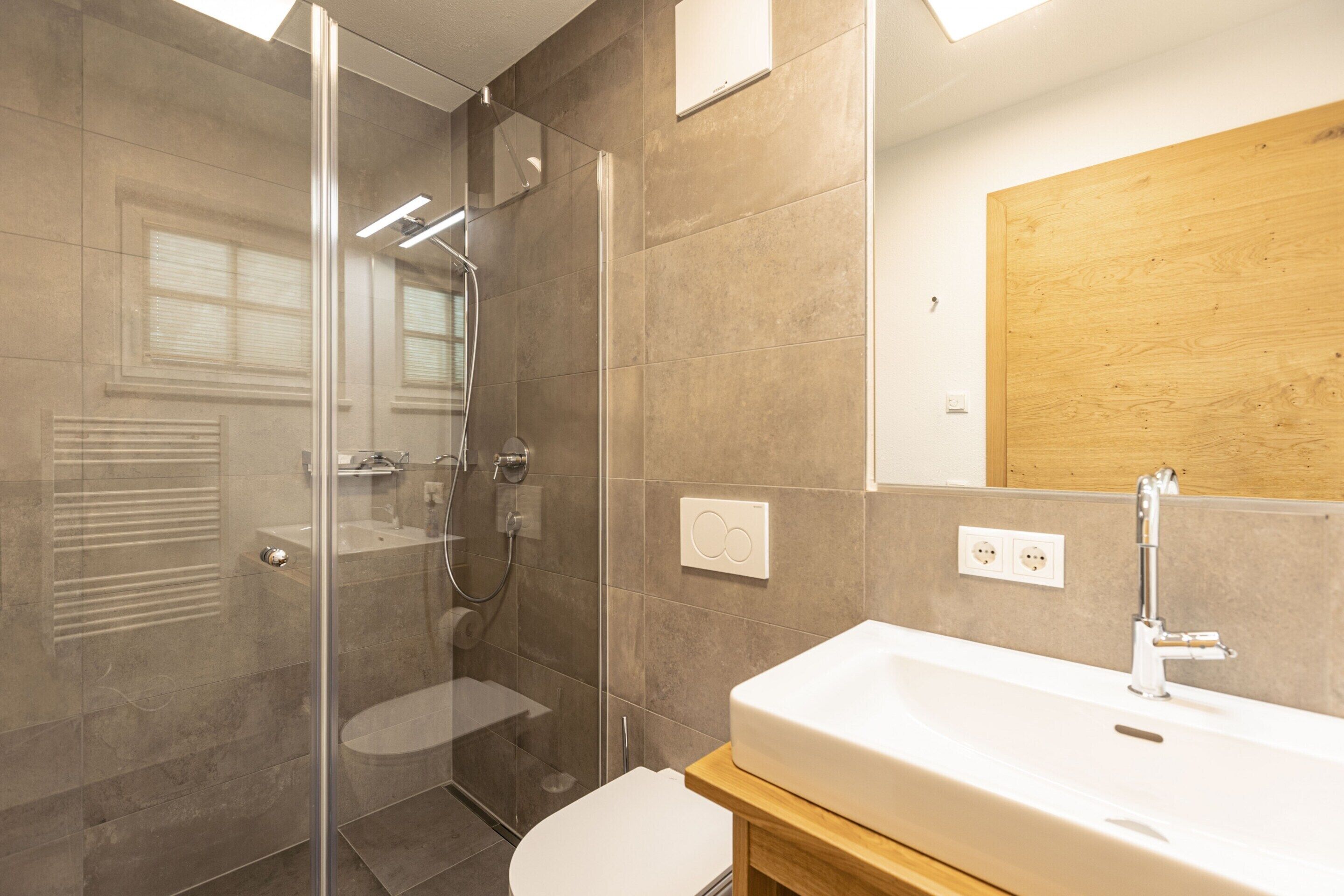 Un bagno moderno con box doccia in vetro, lavandino bianco e mobile vanitario in legno.