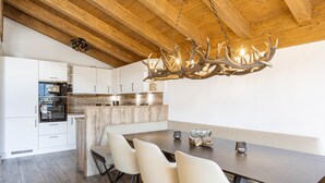 Una cocina moderna con armarios blancos, una mesa de comedor de madera oscura y una lámpara de araña con forma de asta de ciervo.