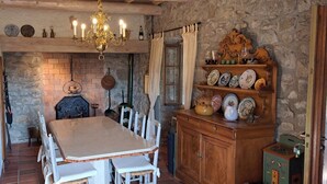 A rustic dining area with a stone wall, wooden furniture, and a chandelier. - The Mas of Largellas (Balazuc)