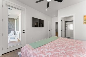 Un dormitorio con cama, ventilador de techo, manta verde y vista a un patio con sillas y un muro de piedra.