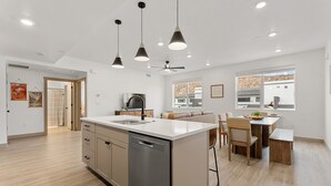 A modern kitchen with a central island, pendant lighting, and a dining area with a table and chairs. - Copper House 2 Bedroom Condo (Hurricane)