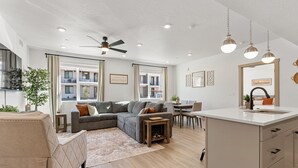 A modern living room with a sectional sofa, a dining area, and a kitchen island. - Pinyon Pines #103 2 Bedroom Condo (Hurricane)