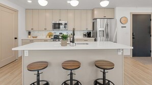 A modern kitchen with a central island, bar stools, and pendant lighting. - Pinyon Pines #103 2 Bedroom Condo (Hurricane)