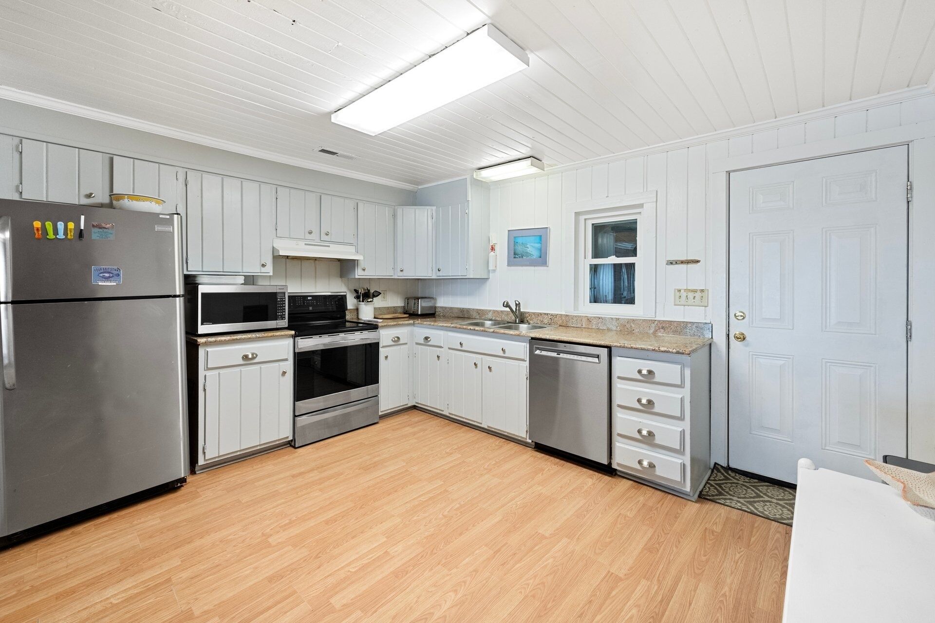 A kitchen with white cabinetry, stainless steel appliances, and a wooden floor.