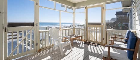 A covered deck with a view of the ocean, wooden chairs, and a table.