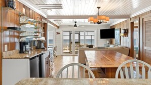 A modern kitchen with granite countertops, a dining area with a wooden table and chairs, and a view of the ocean through large sliding doors.