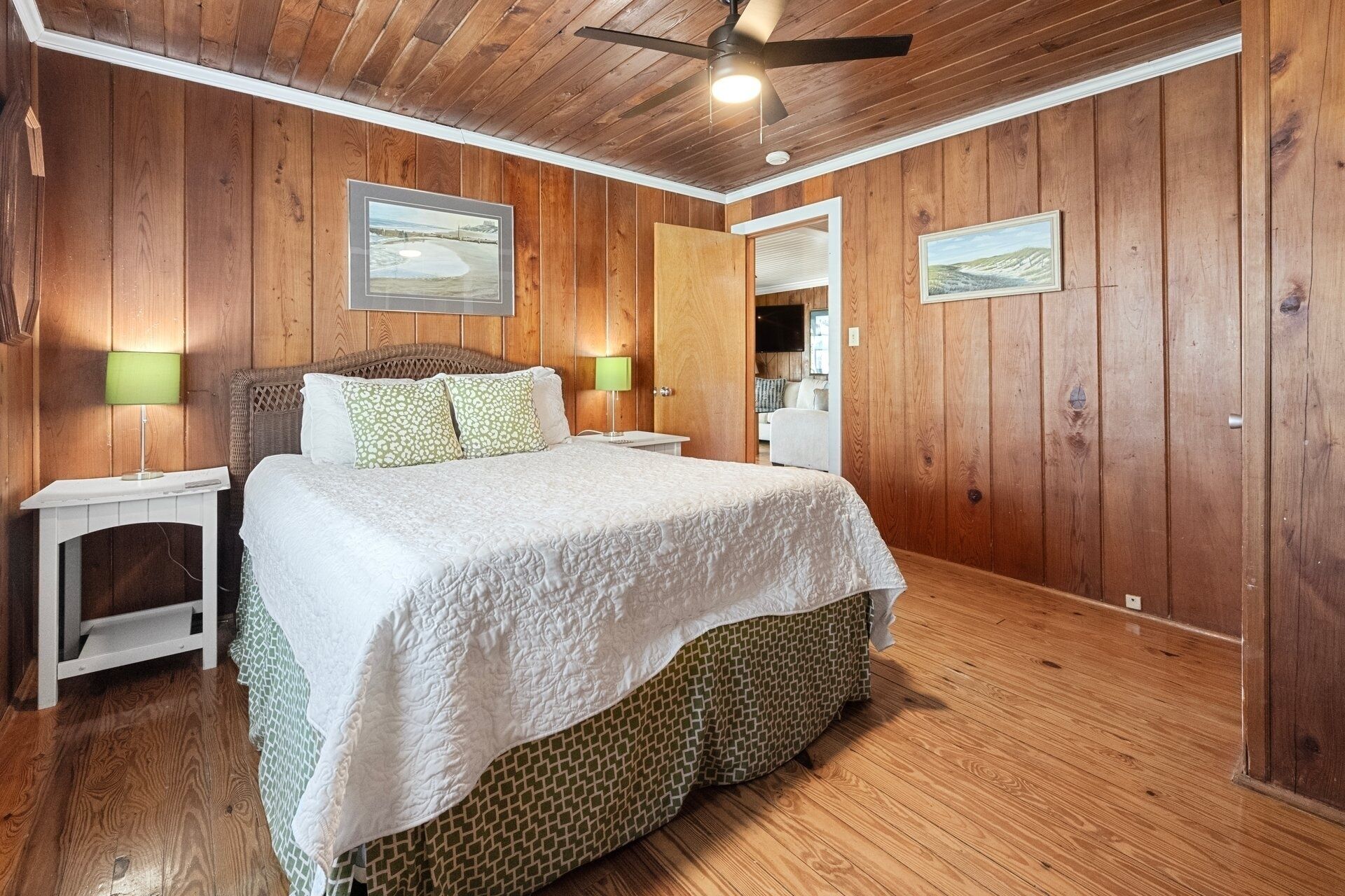 A wooden-paneled bedroom with a bed, two bedside lamps, and two framed pictures on the walls.