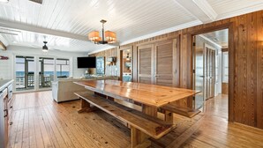 A spacious living area with a large wooden dining table, a comfortable sofa, and a television mounted on the wall.