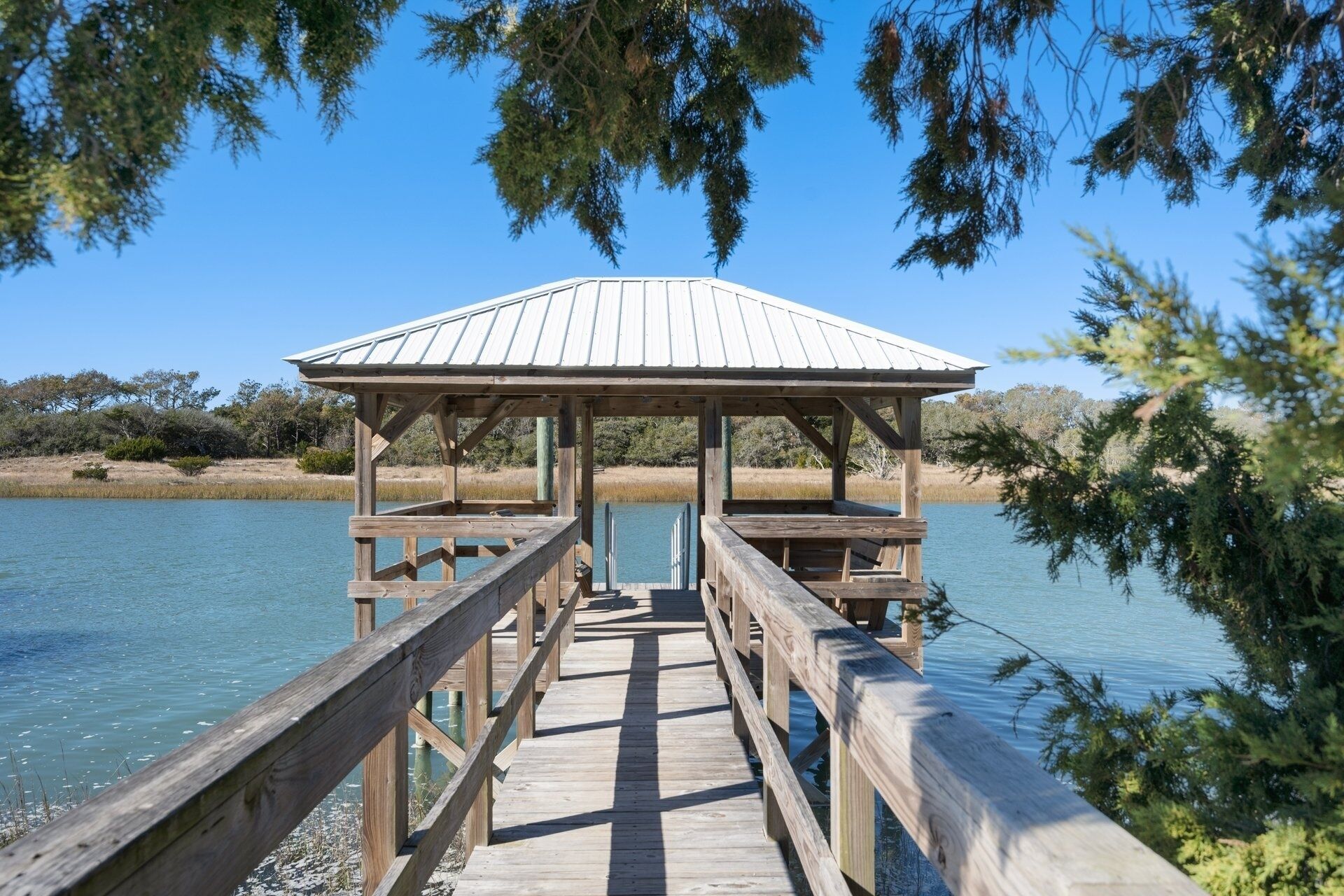 A wooden pier leading to a gazebo over a body of water, surrounded by trees and shrubs.