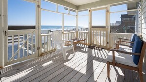 Eine überdachte Terrasse mit Blick auf das Meer, Holzstühle und ein Tisch.