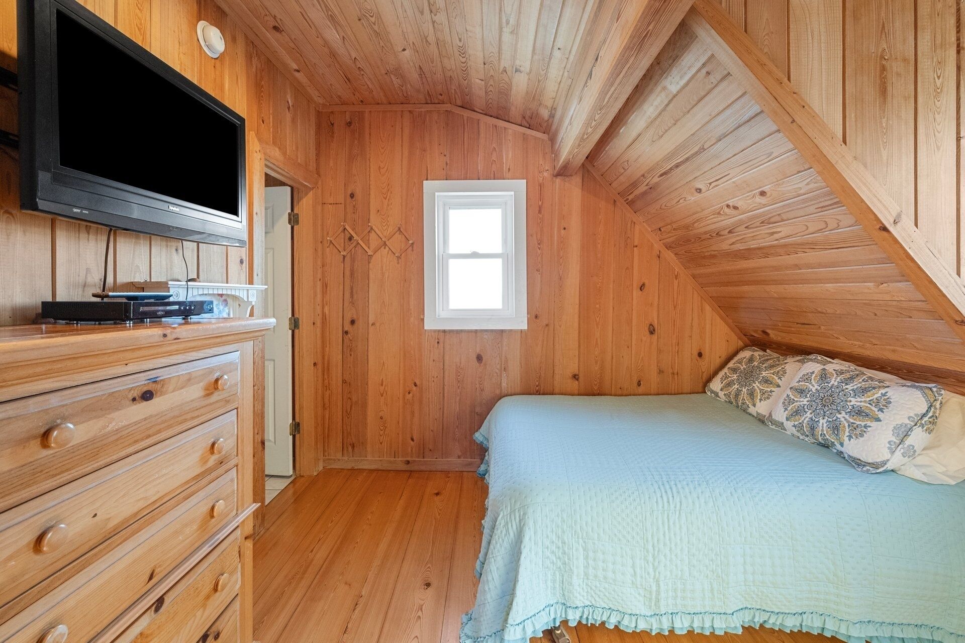A wooden room with a bed, a dresser, and a TV mounted on the wall.