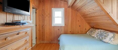 A wooden room with a bed, a dresser, and a TV mounted on the wall.
