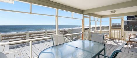 A covered outdoor area with a table and chairs, overlooking a beach.