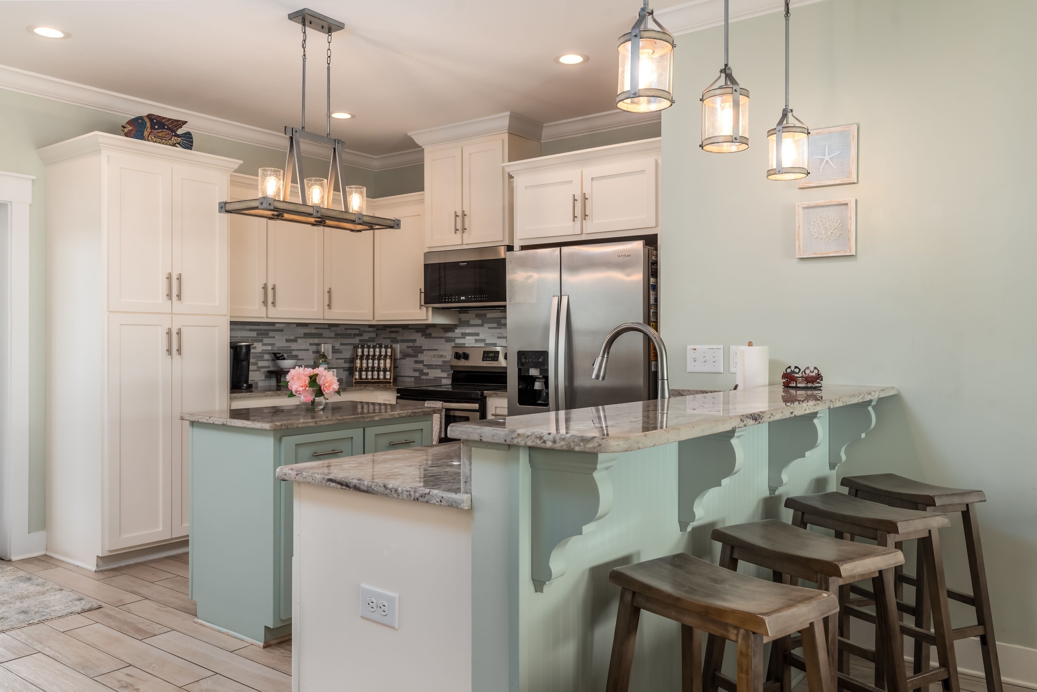 A modern kitchen with white cabinets, a stainless steel refrigerator, and a central island with bar stools.