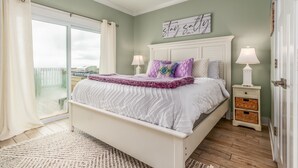 Une chambre à coucher avec un lit, deux tables de chevet avec des lampes, une fenêtre avec des rideaux et un tableau décoratif au mur.
