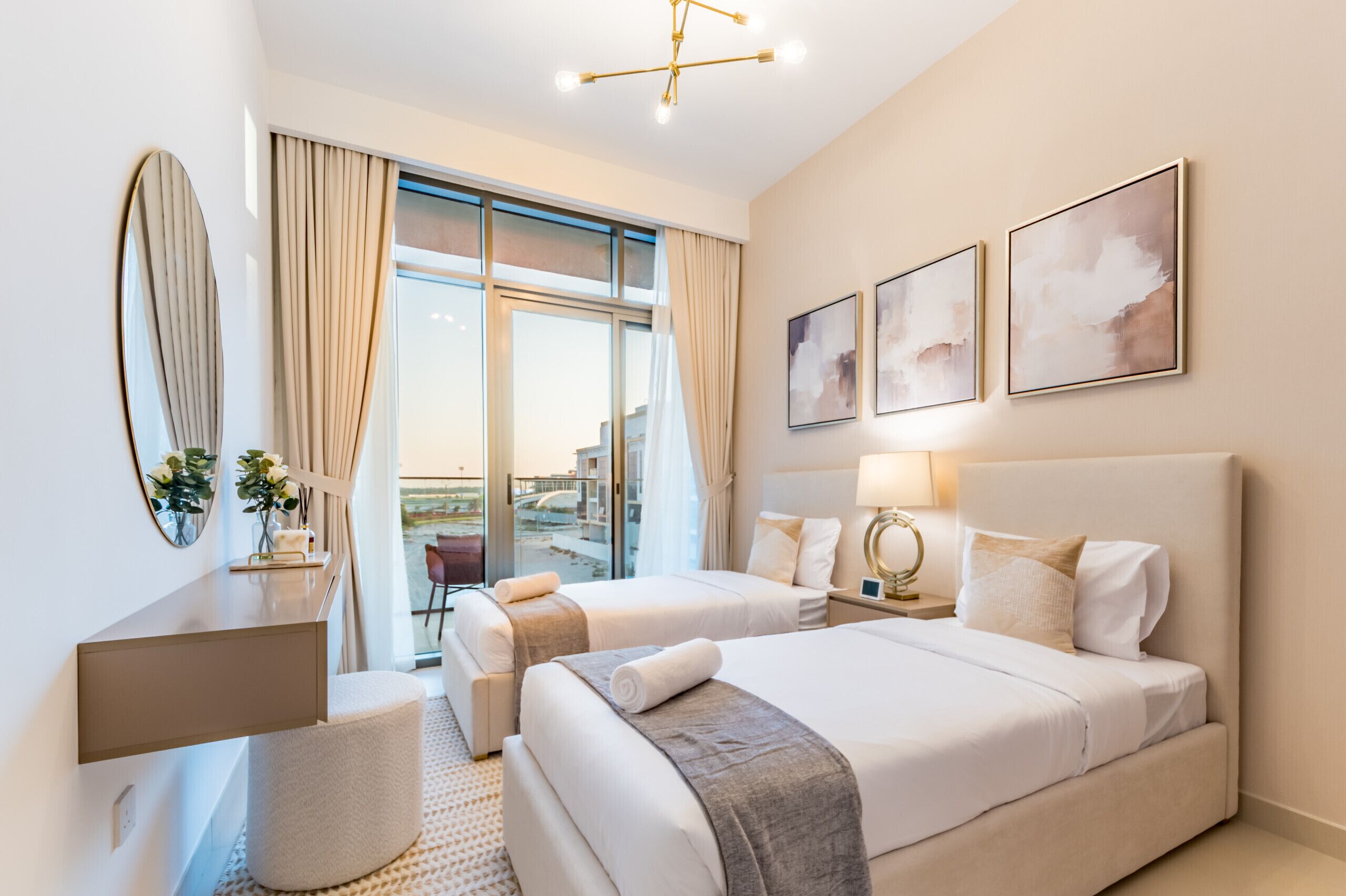 A hotel room with two beds, a desk, a chair, a large window with curtains, and artwork on the wall.