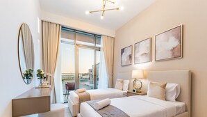 A hotel room with two beds, a desk, a chair, a large window with curtains, and artwork on the wall. - Contemporary 2BR in Azizi Park Avenue, Nad Al Sheba by Deluxe Holiday Homes (Dubai)