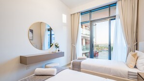 A modern hotel room with a large window, a round mirror, a bedside table, and a bed with white linens. - Contemporary 2BR in Azizi Park Avenue, Nad Al Sheba by Deluxe Holiday Homes (Dubai)