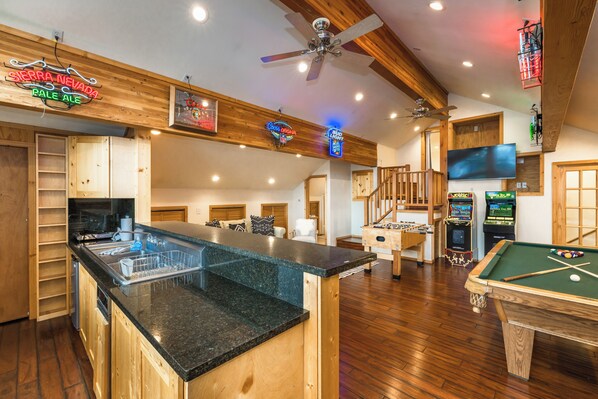 A spacious room with a pool table, a bar area with a neon sign, and a ceiling fan. - Hawk Haven_Hot Tub, Hydronic Heat, Game Room w/ Pool Table, Foosball, Arcades, 2790sqft (Truckee)