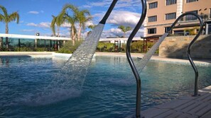 A swimming pool with clear water, surrounded by palm trees and a modern building in the background. - Mayim Hotel Termal & SPA (Concordia)
