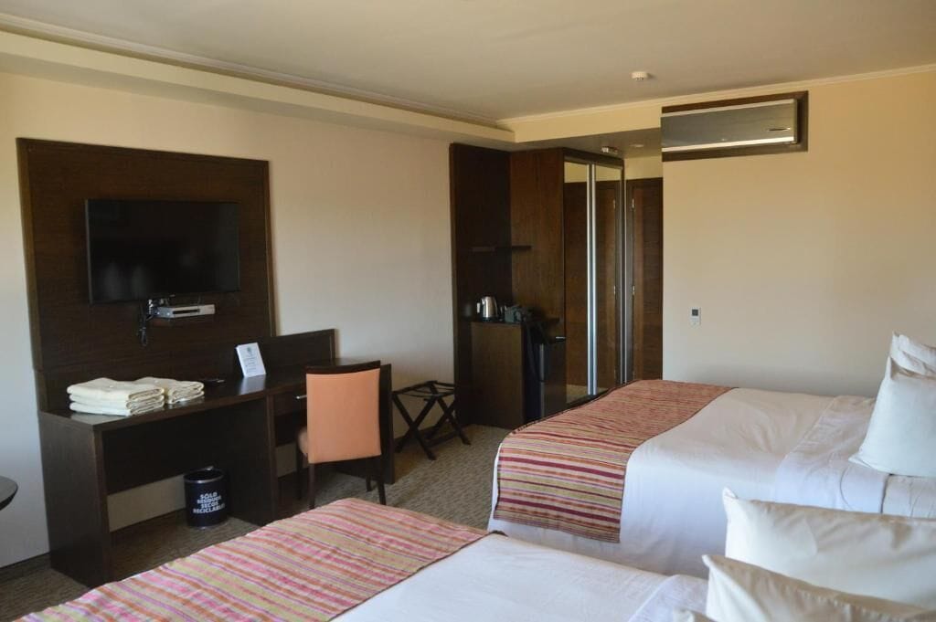 A hotel room with two beds, a desk with a chair, a television, and a mirror.