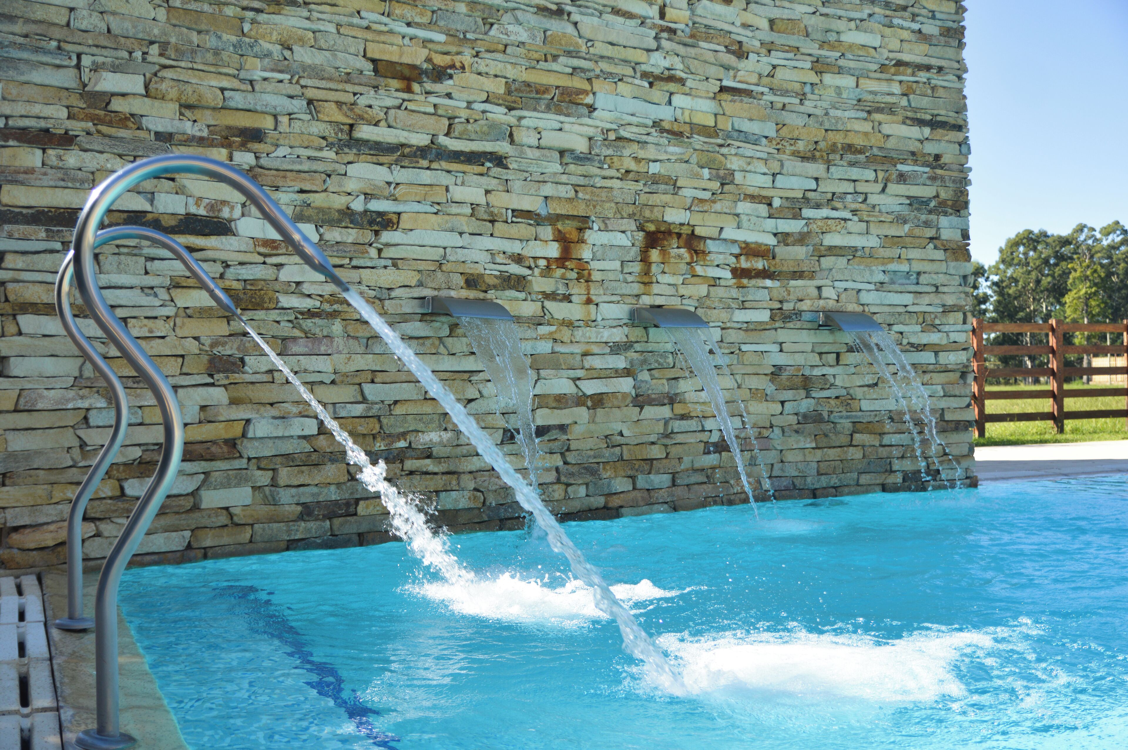A stone wall with a pool and metal handrails.