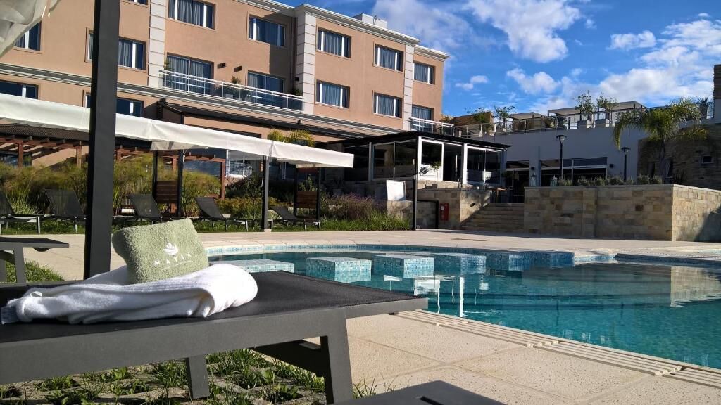 Ein Poolbereich mit Liegestühlen und einem Handtuch, ein Gebäude mit mehreren Balkonen und einem wolkenlosen Himmel.
