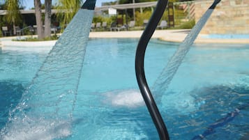 Une piscine avec une rambarde métallique, une eau d’un bleu limpide, des palmiers et un bâtiment en arrière-plan.