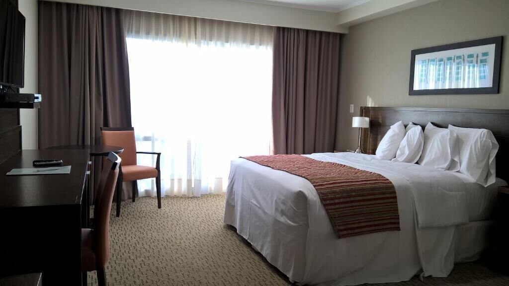 A hotel room with a bed, a desk, a chair, and a window with curtains.