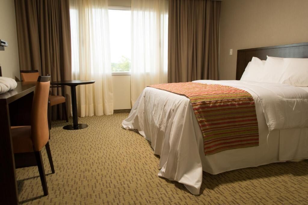 Una habitación de hotel con cama, escritorio, silla y ventana con cortinas.