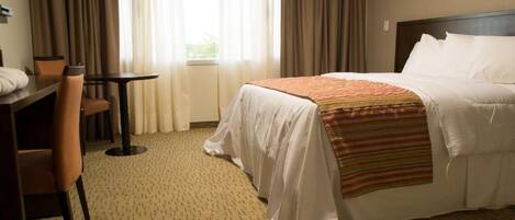 Una habitación de hotel con cama, escritorio, silla y ventana con cortinas.