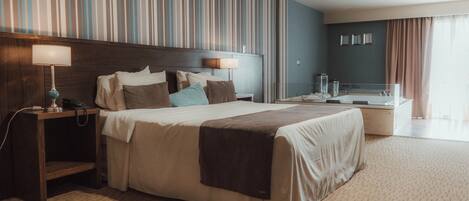 A hotel room with a large bed, bedside lamps, a nightstand, a desk with a computer, a mirror, and a bathroom with a bathtub.