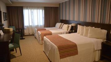 A hotel room with two beds, a desk, a chair, and a view of the street through curtains.