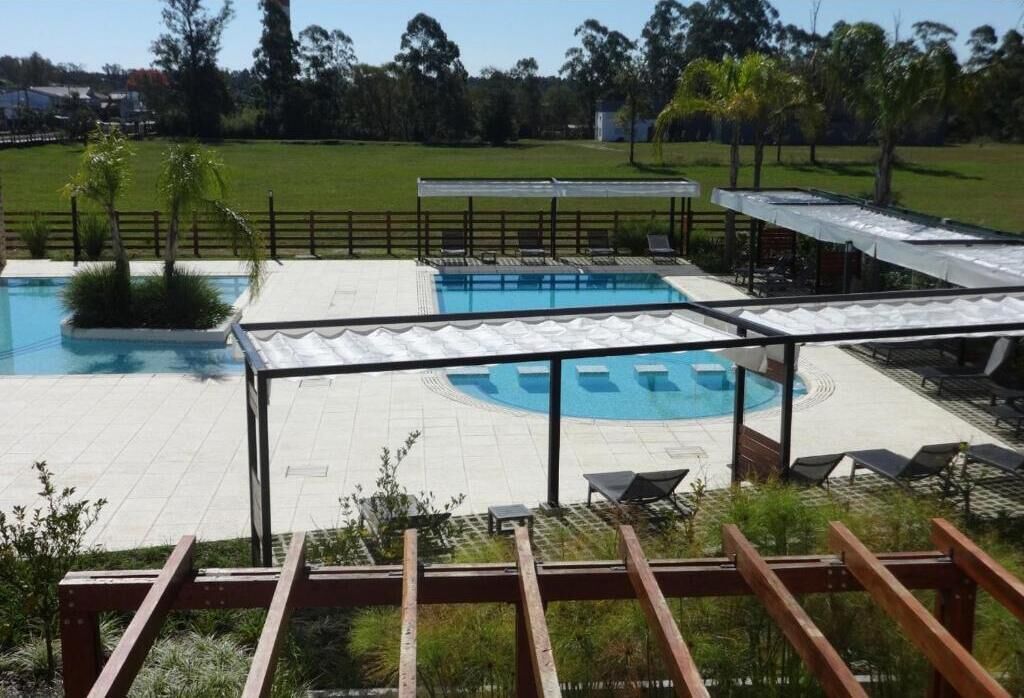 Un área de piscina con varias piscinas, tumbonas y una zona de estar cubierta.
