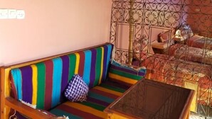 Una habitación acogedora con un sofá a rayas de colores, una mesita de madera y una cama con un cabecero decorativo.