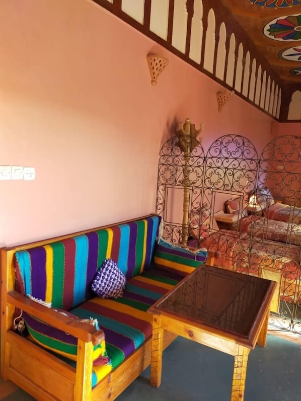 Una habitación acogedora con un sofá a rayas de colores, una mesita de madera y una cama con un cabecero decorativo.