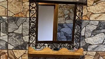 Un baño con pared de estilo piedra, un lavamanos blanco y un espejo decorativo con marco de metal.