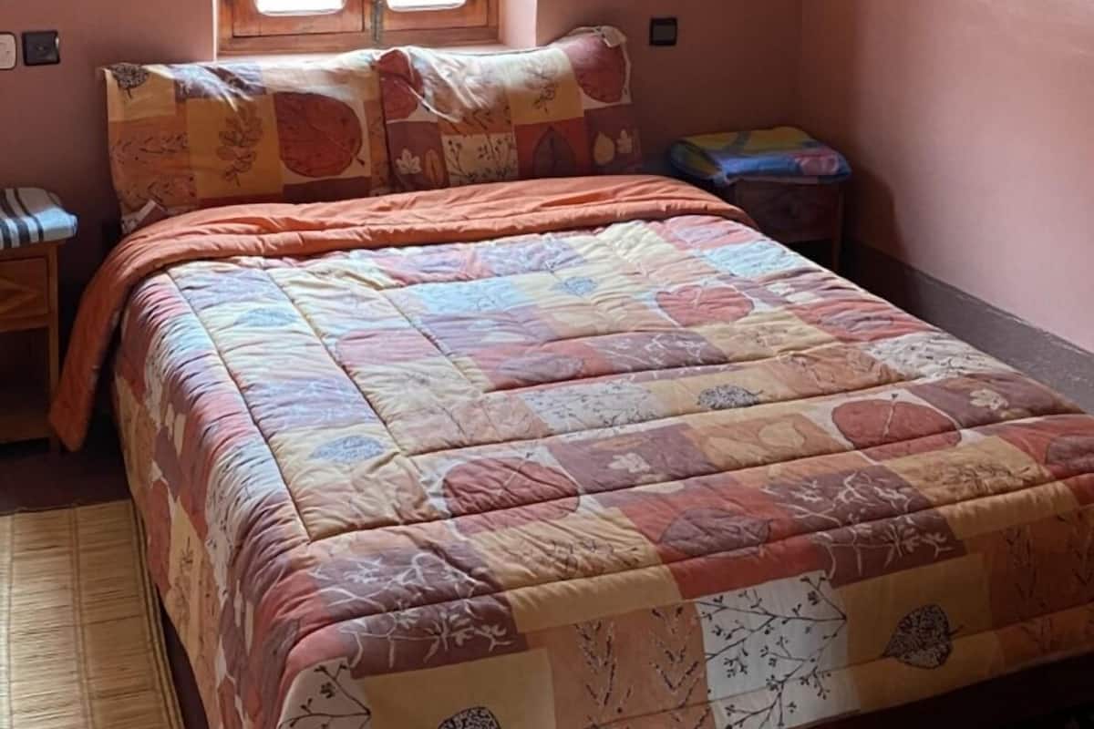 A bedroom with a bed, a window, a nightstand, and a wall-mounted light fixture.