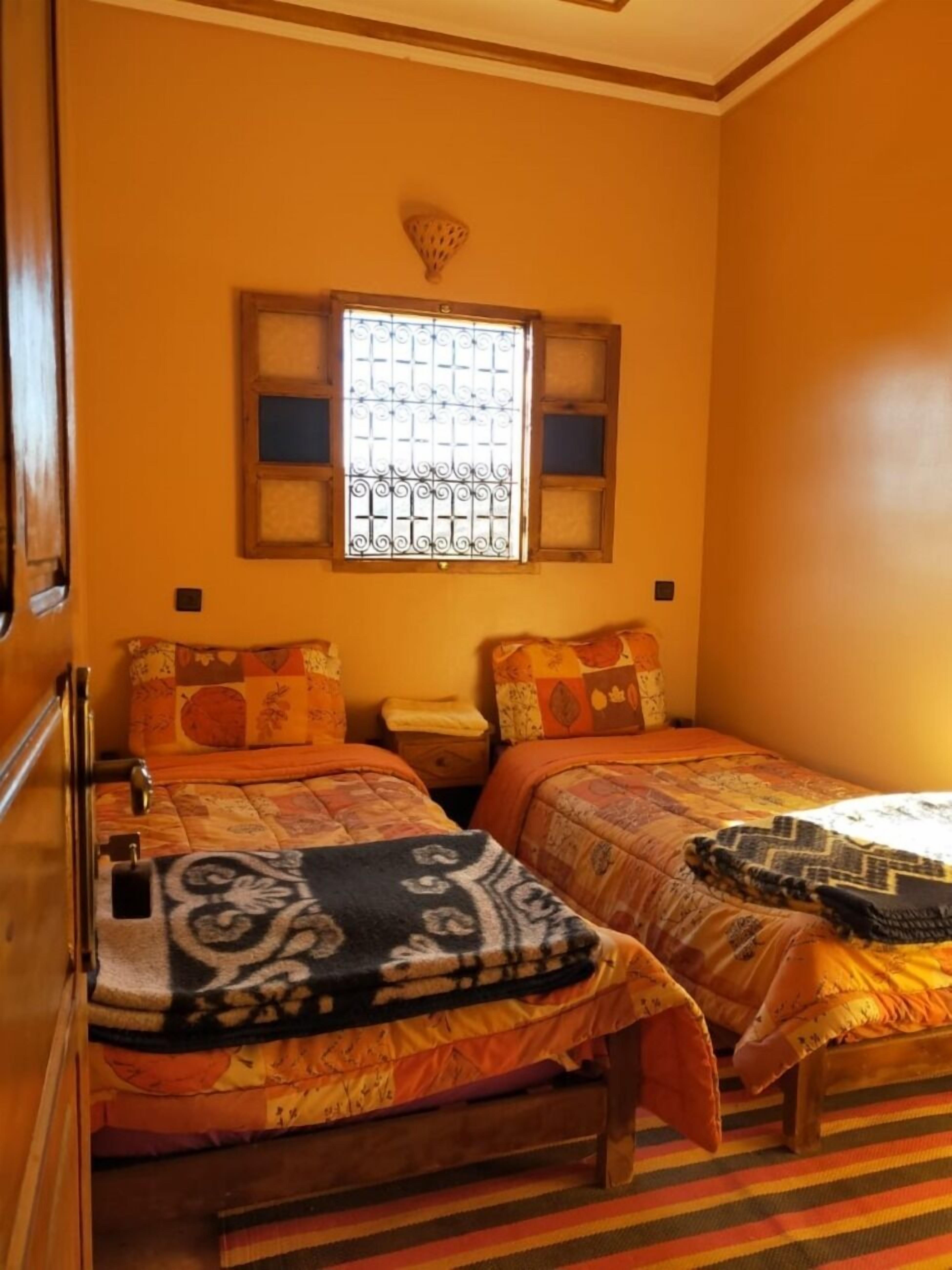 A room with two beds, a window with decorative iron bars, and a striped rug on the floor.