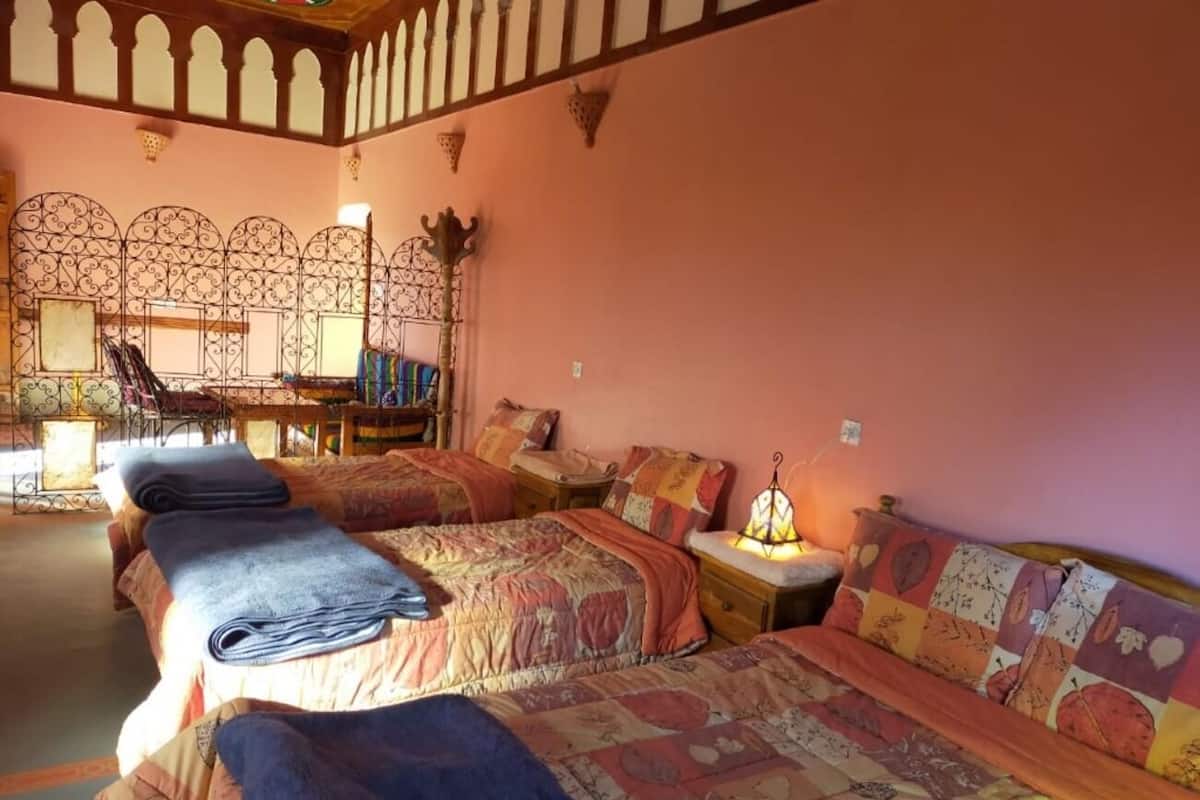 A room with two beds, each with a patterned bedspread and pillows, a nightstand with a lamp, and a decorative wall with a geometric pattern.