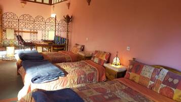 A room with two beds, each with a patterned bedspread and pillows, a nightstand with a lamp, and a decorative wall with a geometric pattern.