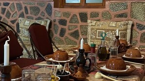 Una mesa de comedor dispuesta con cerámica y utensilios tradicionales, una ventana y una pared con diseño de piedra.