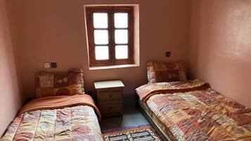 Un dormitorio pequeño con dos camas individuales, una mesita de noche, una ventana y un interruptor de luz en la pared.