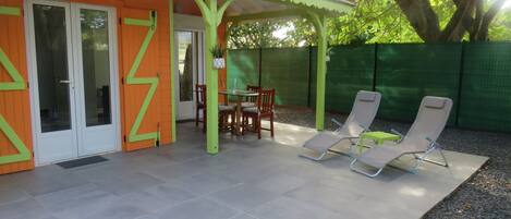Relax in a serene outdoor space with a patio table and two lounge chairs, surrounded by a green fence and a tiled floor.