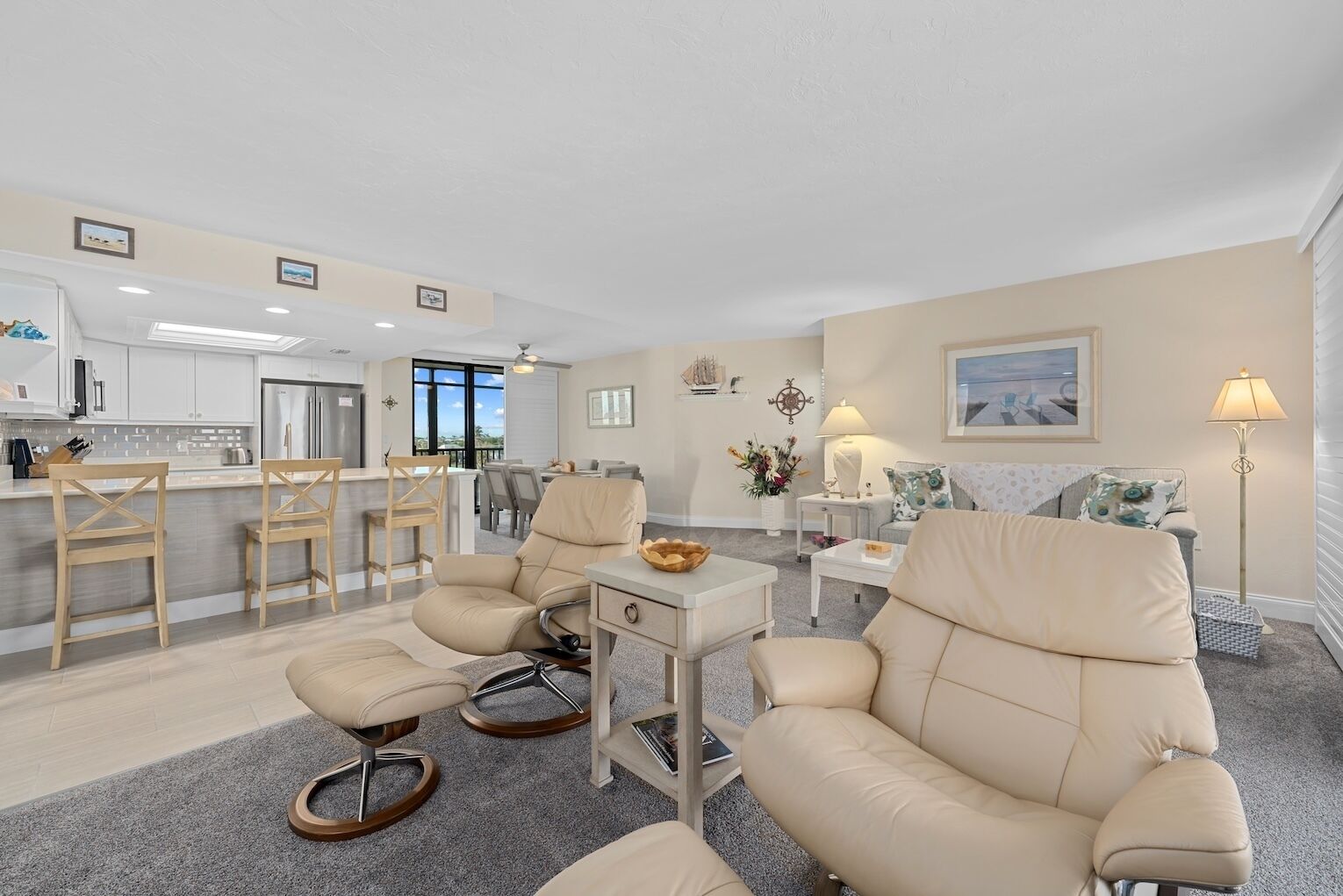A modern living room with a sofa, chairs, and a dining area with a kitchen in the background.