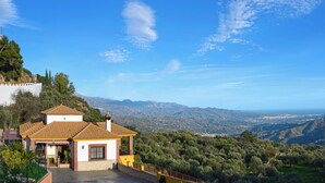 A house with a tiled roof, white walls, and a stone foundation. It is surrounded by greenery and overlooks a valley with mountains in the distance. - Fabulous villa, airco, pool, WIFI. Walking distance to village. Amazing views. (Comares)