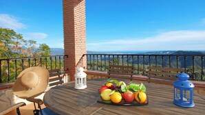 A wooden deck with a brick pillar, a bench, a table with fruit, and lanterns. - Fabulous villa, airco, pool, WIFI. Walking distance to village. Amazing views. (Comares)