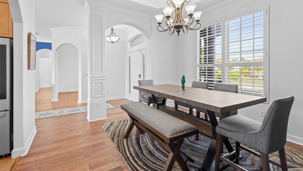 A dining area with a wooden table, bench, and chairs, a chandelier, and a view through a window with blinds. - Lakewood Ranch–Spacious 3BR Home with Den by RVA (Bradenton)