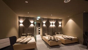 Ein moderner Spa-Raum mit drei Liegen, Holzpaneelen an den Wänden und indirekter Beleuchtung.